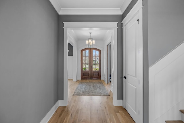 interior space with baseboards, ornamental molding, french doors, light wood-type flooring, and a chandelier