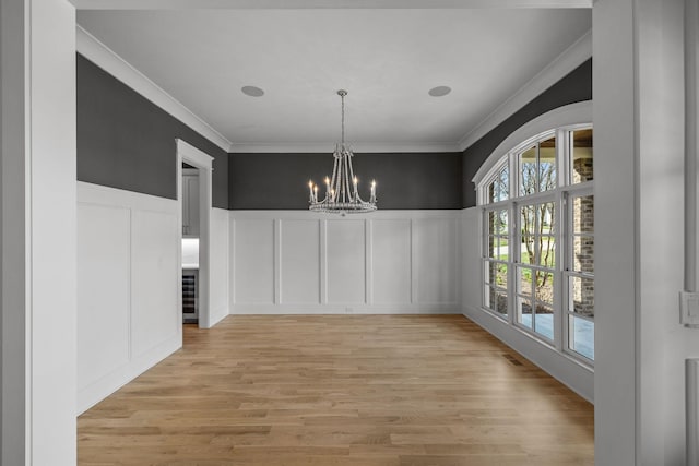 unfurnished dining area featuring crown molding, a decorative wall, and light wood-type flooring