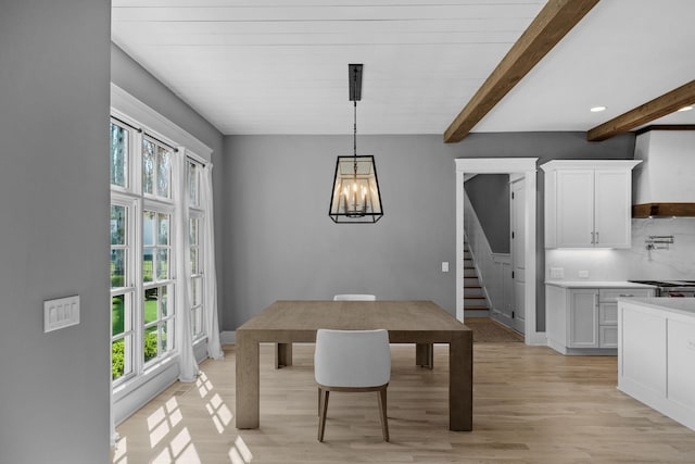 dining room with beam ceiling, a notable chandelier, light wood-style flooring, baseboards, and stairs