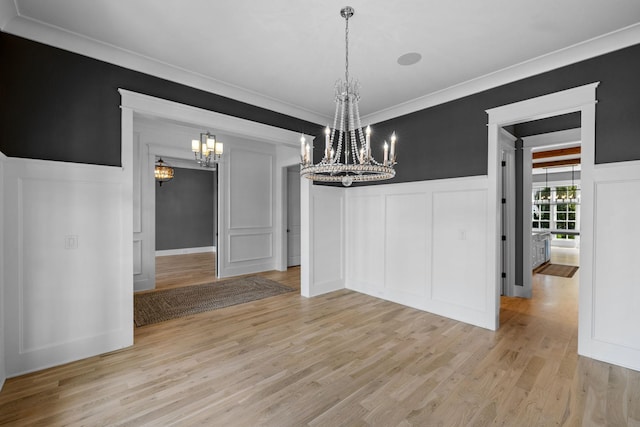 unfurnished dining area with a decorative wall, ornamental molding, wainscoting, light wood-style floors, and a notable chandelier