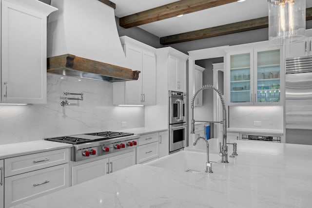 kitchen with backsplash, premium range hood, beam ceiling, appliances with stainless steel finishes, and white cabinets