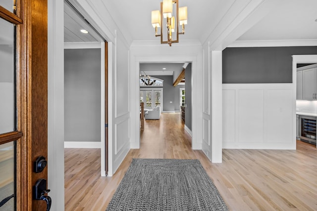 foyer entrance featuring light wood-type flooring, ornamental molding, wine cooler, an inviting chandelier, and a decorative wall