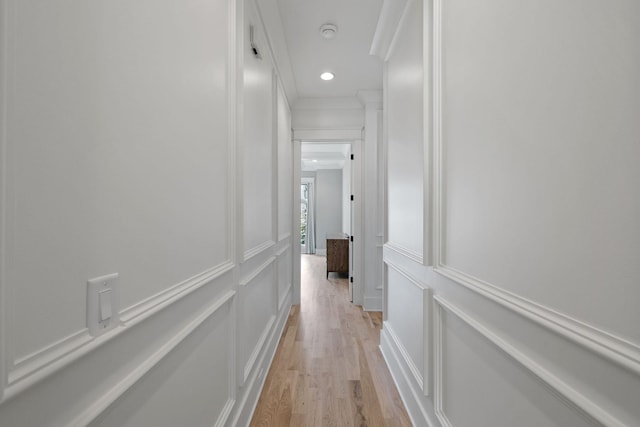 hallway featuring light wood finished floors, a decorative wall, and crown molding