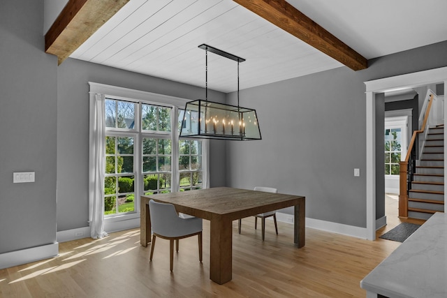 dining space with light wood-type flooring, stairway, a healthy amount of sunlight, and beamed ceiling