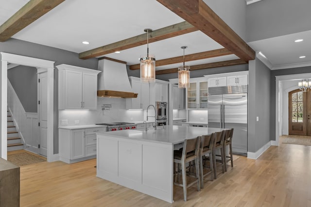 kitchen featuring stainless steel appliances, custom exhaust hood, white cabinets, and light wood finished floors