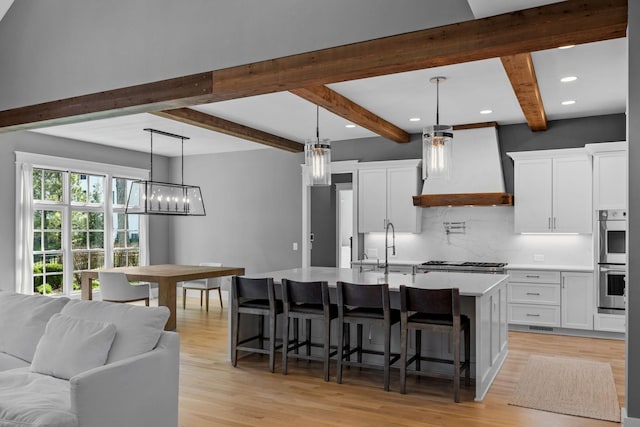 kitchen with a breakfast bar, light countertops, custom range hood, appliances with stainless steel finishes, and a sink