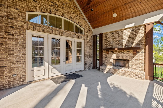 view of exterior entry with french doors, a patio, brick siding, and an outdoor brick fireplace