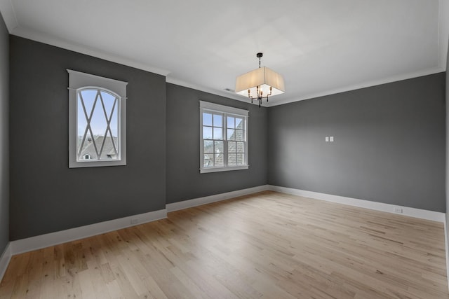 empty room with an inviting chandelier, light wood-style floors, baseboards, and ornamental molding