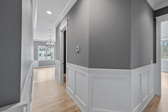 hallway featuring a decorative wall, light wood-style flooring, an inviting chandelier, and a wainscoted wall