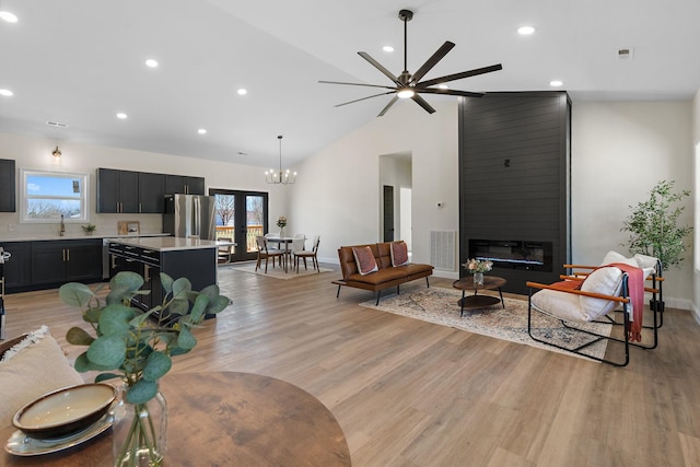 living room with light wood finished floors, plenty of natural light, ceiling fan with notable chandelier, and a fireplace