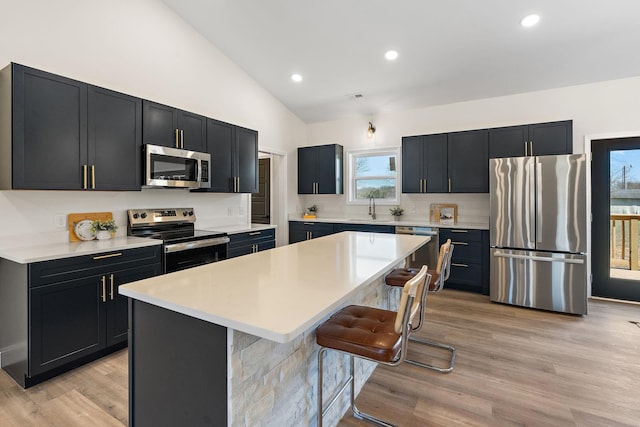 kitchen with dark cabinetry, a kitchen island, stainless steel appliances, vaulted ceiling, and light countertops