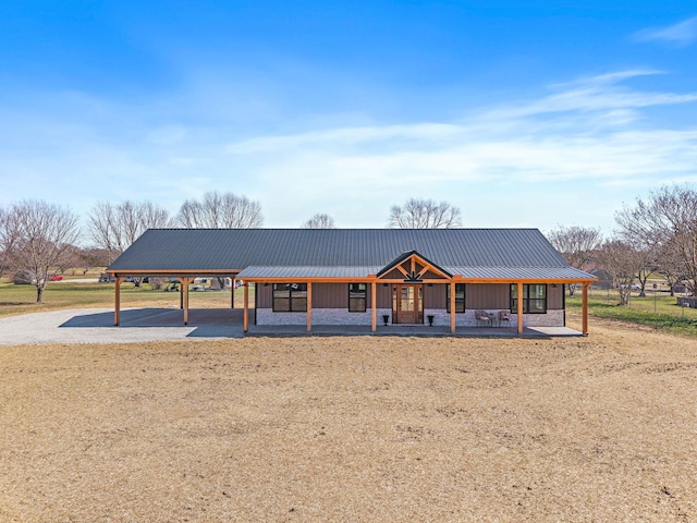 farmhouse-style home with an attached carport, a porch, metal roof, stone siding, and driveway