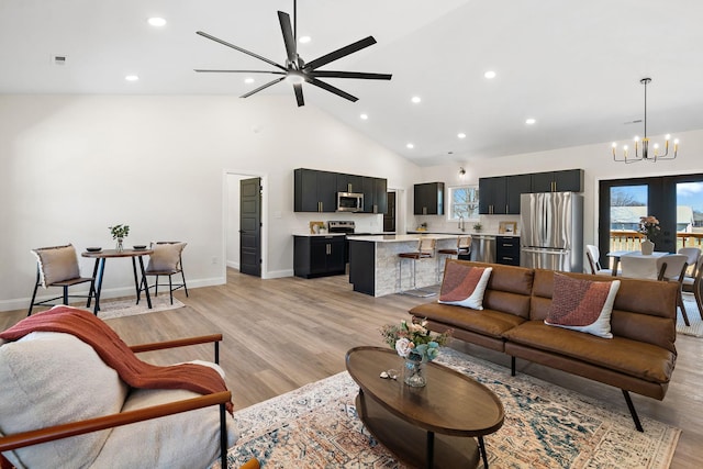 living area with recessed lighting, ceiling fan with notable chandelier, light wood finished floors, and high vaulted ceiling