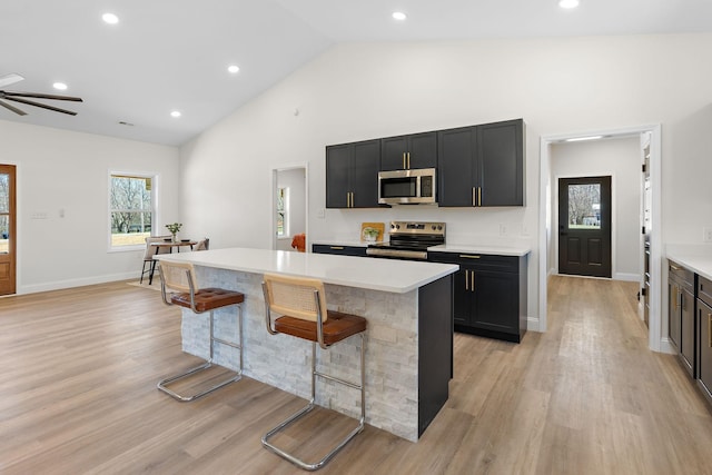 kitchen with a breakfast bar, light wood-style floors, appliances with stainless steel finishes, light countertops, and dark cabinets