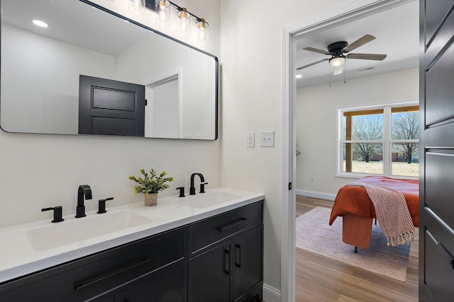 ensuite bathroom with a sink, double vanity, wood finished floors, and a ceiling fan