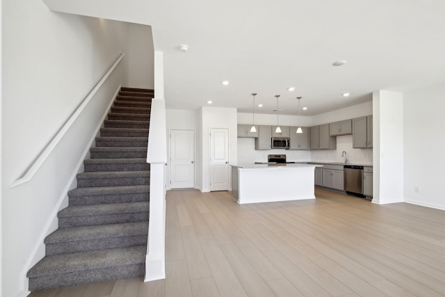 kitchen featuring light wood finished floors, stainless steel appliances, baseboards, gray cabinetry, and light countertops