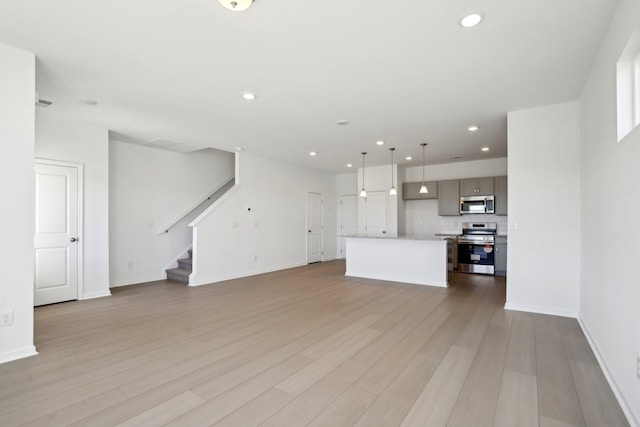 unfurnished living room with recessed lighting, light wood-style flooring, stairs, and baseboards