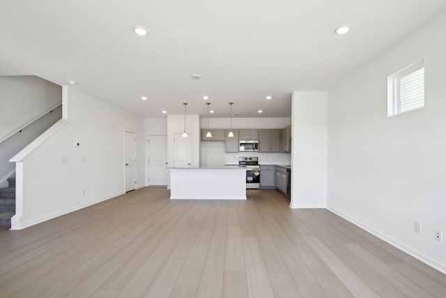 unfurnished living room featuring recessed lighting, light wood-type flooring, baseboards, and stairs