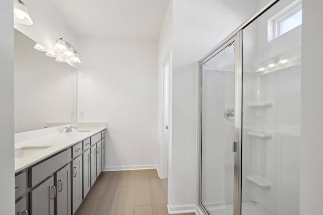 full bathroom with baseboards, a sink, a shower stall, and double vanity
