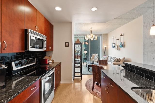 kitchen with dark stone countertops, light wood finished floors, stainless steel appliances, decorative backsplash, and a chandelier