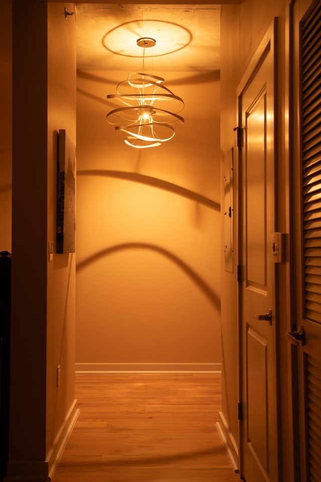 corridor featuring wood finished floors, baseboards, and a chandelier