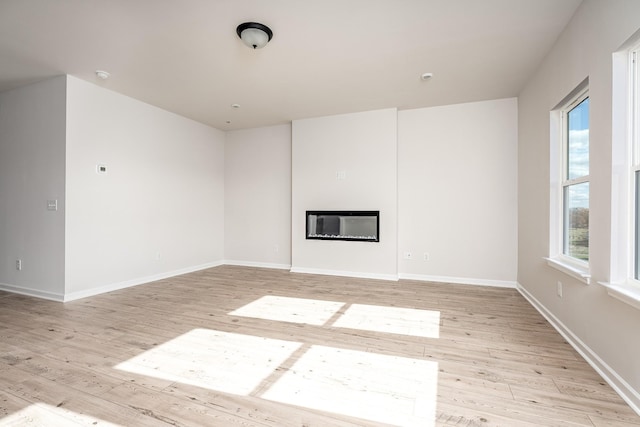 empty room with a glass covered fireplace, baseboards, and light wood-style floors