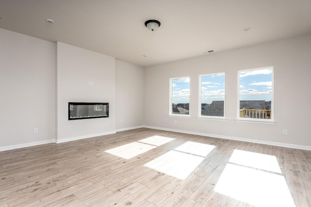 unfurnished living room featuring visible vents, baseboards, light wood-style floors, and a glass covered fireplace