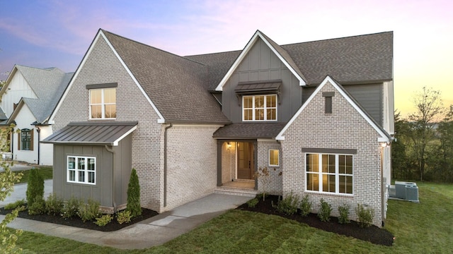 view of front facade with roof with shingles, a front lawn, board and batten siding, central air condition unit, and brick siding