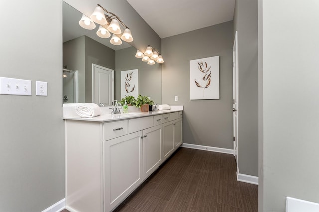 bathroom with double vanity, a shower with door, baseboards, and a sink