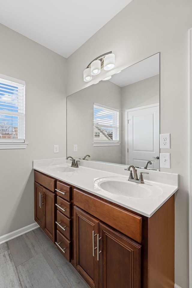 full bath with double vanity, wood finished floors, baseboards, and a sink