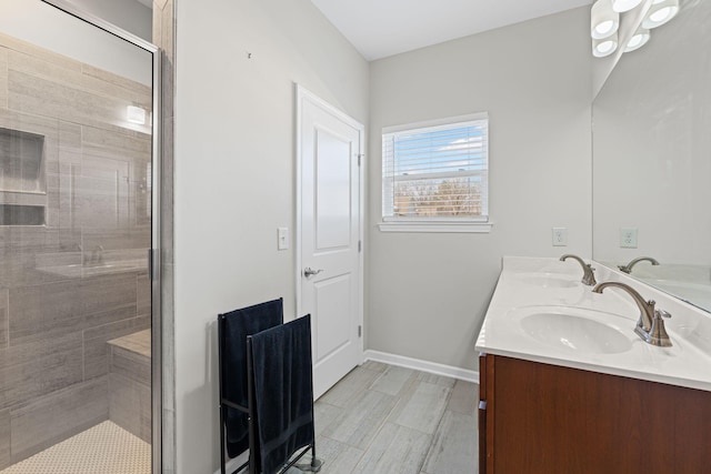 full bath featuring a shower stall, double vanity, baseboards, and a sink