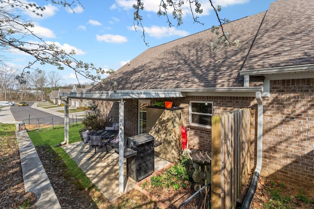 exterior space with a patio, fence, brick siding, and a shingled roof