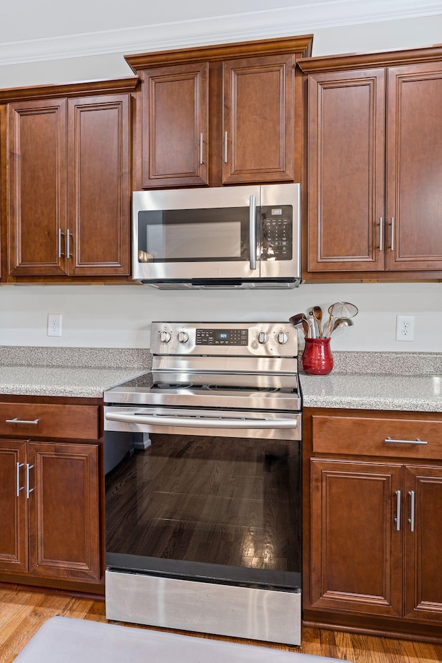 kitchen featuring light wood-type flooring, appliances with stainless steel finishes, crown molding, and light countertops