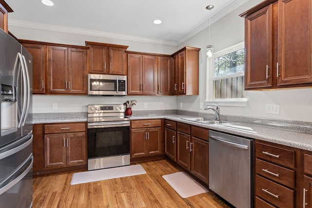 kitchen with a sink, light wood-style floors, appliances with stainless steel finishes, and crown molding