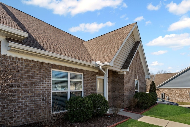 view of property exterior featuring brick siding, roof with shingles, and a lawn