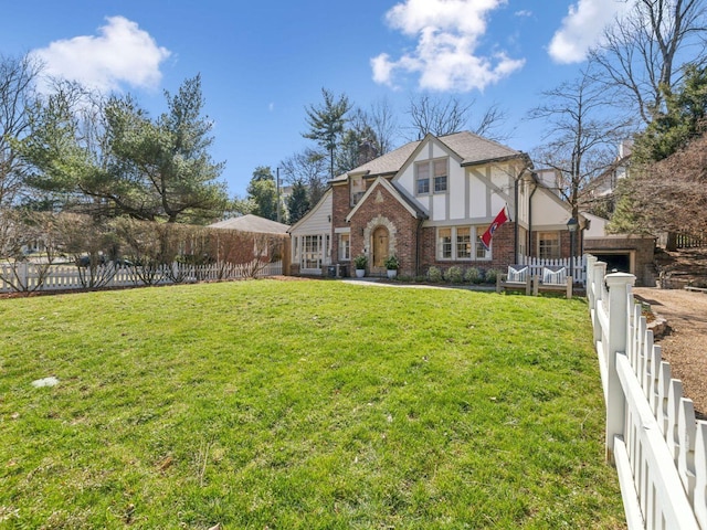 english style home featuring a front yard, fence, brick siding, and stucco siding