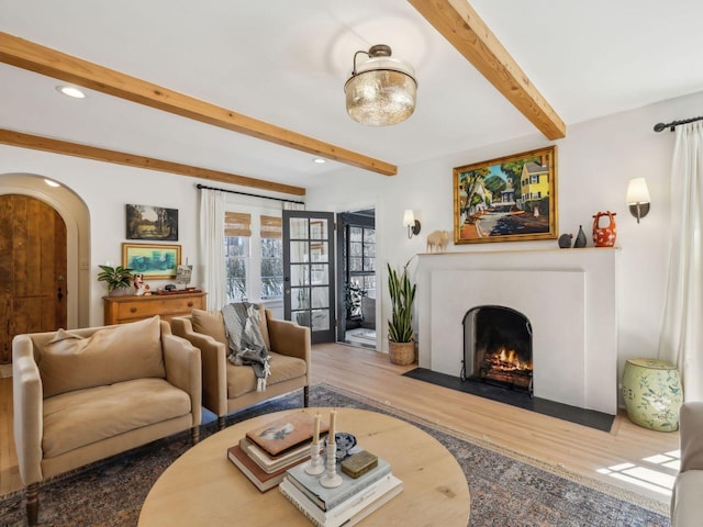 living room with wood finished floors, a fireplace with flush hearth, recessed lighting, arched walkways, and beamed ceiling