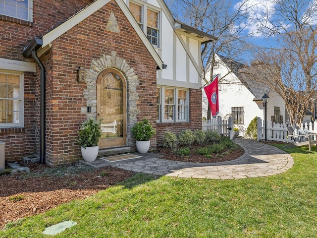 view of exterior entry featuring brick siding, a yard, and fence