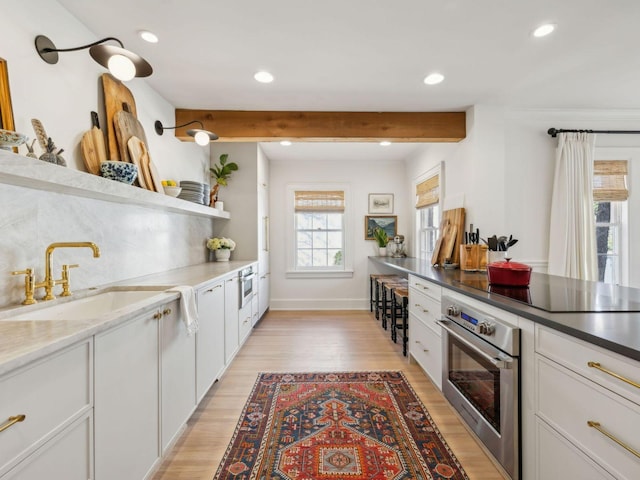 kitchen featuring oven, black electric stovetop, light wood-type flooring, white cabinetry, and a sink