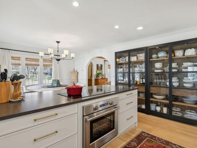 kitchen with oven, dark countertops, electric stovetop, arched walkways, and a chandelier