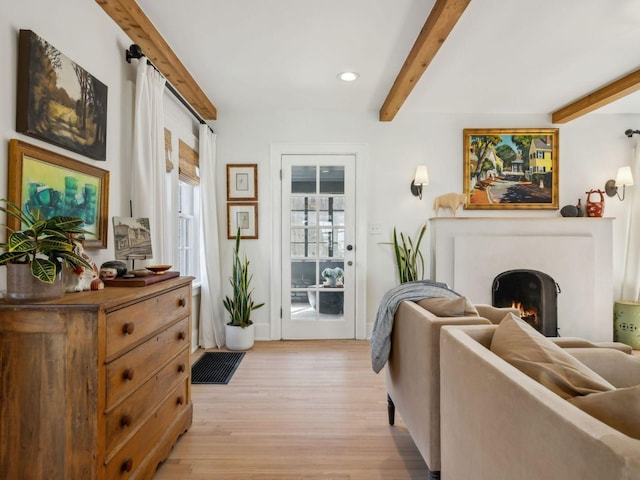 living area featuring beamed ceiling, recessed lighting, a warm lit fireplace, and light wood-style floors