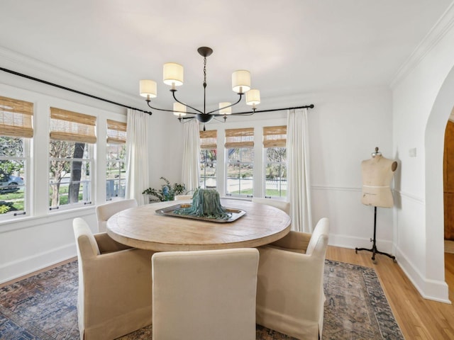 dining space with light wood-type flooring, a notable chandelier, ornamental molding, arched walkways, and baseboards