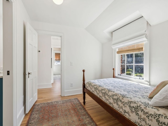 bedroom featuring light wood-type flooring, lofted ceiling, and baseboards