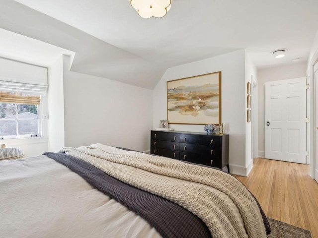 bedroom featuring baseboards, lofted ceiling, and light wood-style floors