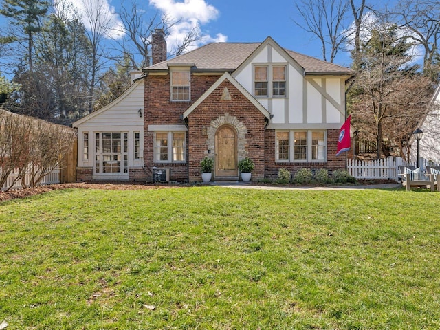 tudor home with brick siding, a chimney, a front lawn, and fence