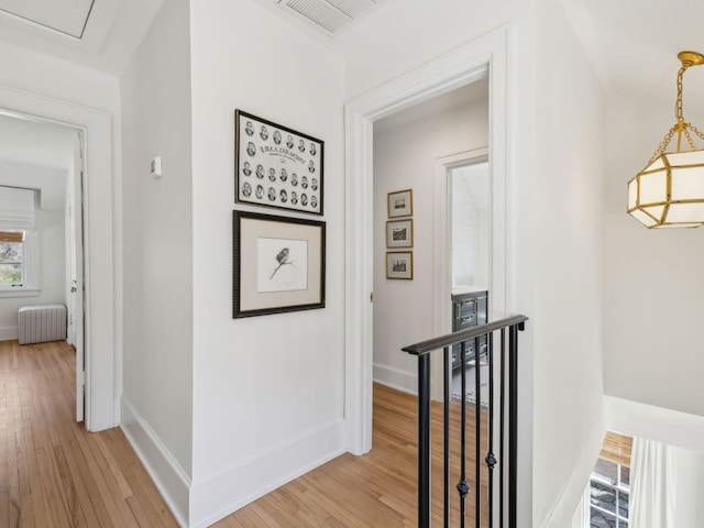 corridor featuring visible vents, baseboards, radiator heating unit, an upstairs landing, and light wood-style floors