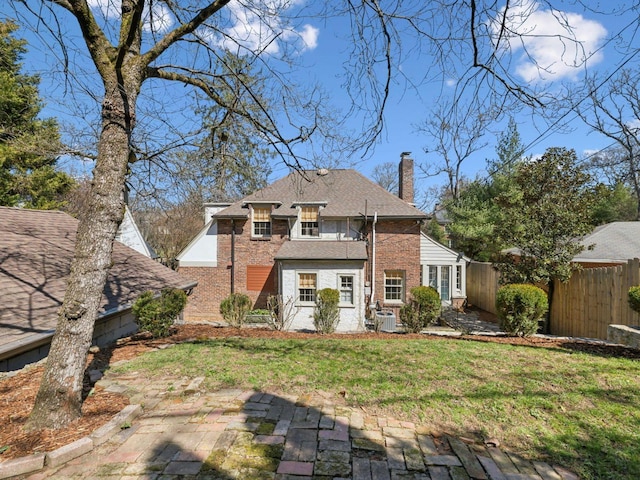 rear view of property with brick siding, a shingled roof, fence, a lawn, and a chimney