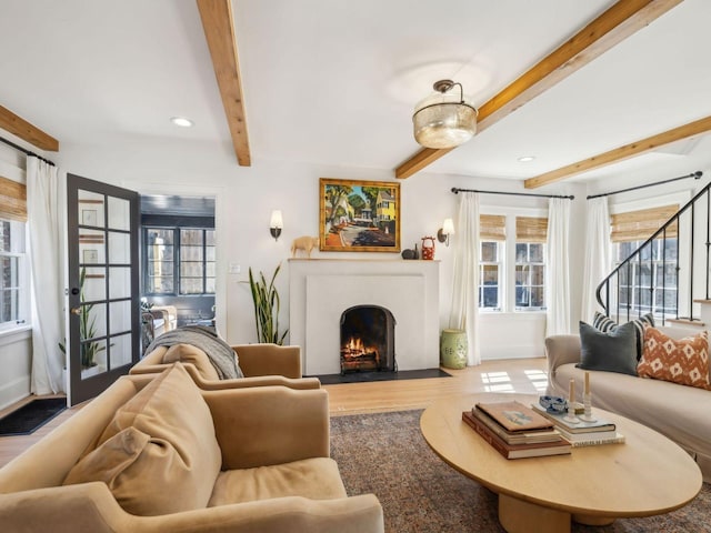 living room featuring plenty of natural light, beam ceiling, wood finished floors, and a fireplace with flush hearth