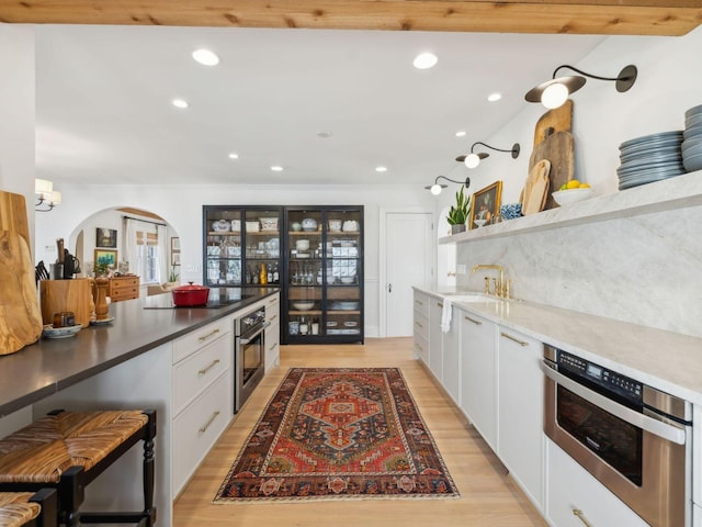 kitchen featuring stainless steel oven, black electric cooktop, arched walkways, and light wood finished floors