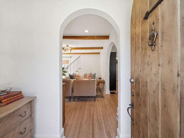 hall featuring beam ceiling, stairway, arched walkways, light wood finished floors, and baseboards